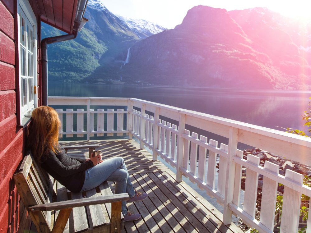 girl sitting near rorbu and admires the beautiful Norwegian landscape at the fjord and mountains